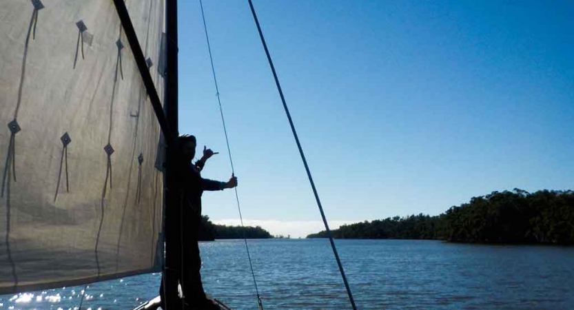 a person gives a hang loose sign while holding a rope on a sailboat on an outward bound expedition
